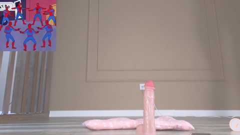 Video of a beige room with a large, realistic pink dildo on a soft pink pillow, surrounded by small blue and red toy soldiers.