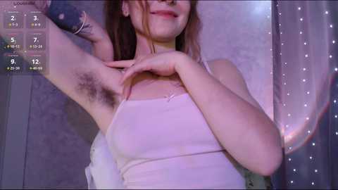 Video of a fair-skinned woman with long brown hair, wearing a white tank top, revealing armpit hair. She stands against a purple, glittery background, with a rating overlay showing 9/12.
