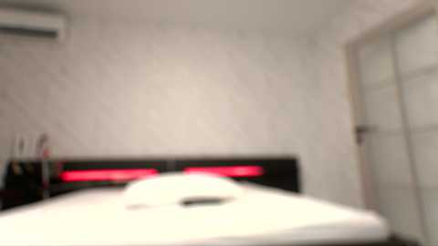 Blurry video of a modern, minimalist bedroom with a white bed, red LED lights under the headboard, white walls, an air conditioning unit, and a sliding glass door.