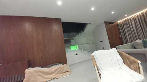 Video of a modern, minimalist bedroom with two wooden headboards, white bedding, and a large window with a green light, creating a serene atmosphere.