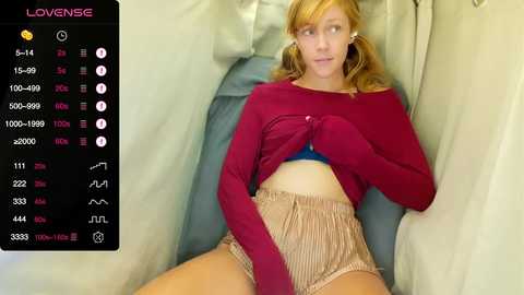 A video of a young, fair-skinned, blonde woman in a red crop top and beige shorts, lying on a blue couch. The image is overlaid with a video player interface showing statistics.