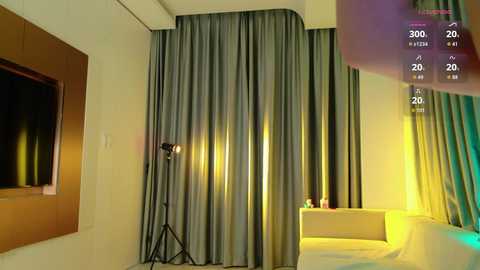 Video of a modern, minimalist hotel room with grey curtains, a white couch, a TV, and a standing lamp.