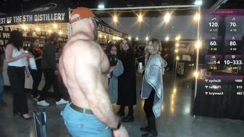 Media: Video of a shirtless, muscular man with a red cap, blue jeans, and a black wristwatch, interacting with a woman in a plaid jacket and leggings at a crowded, dimly-lit bar.