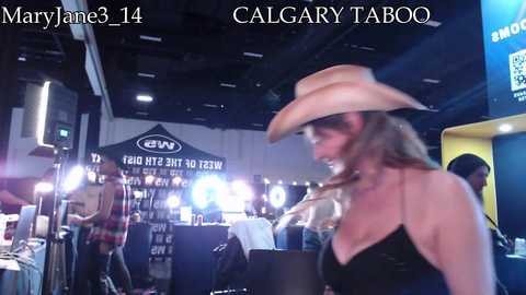 A video captures a smiling woman with light brown hair wearing a cowboy hat and a black top at a dark, modern bar with neon signs and dim lighting.