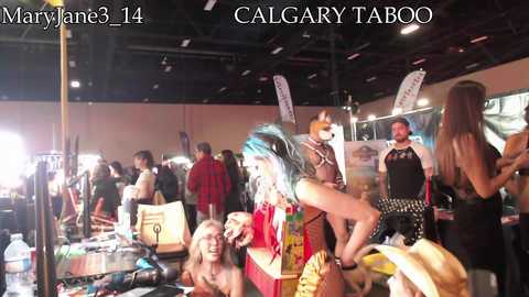 Media: Video of a lively indoor event with a diverse crowd, including people in costumes, at a convention. The background features banners and a mix of casual and themed attire.