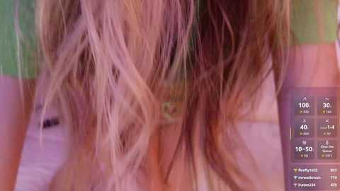 A close-up video of a woman's tousled, wavy, light brown hair, partially covering her face, with a green and pink striped background. An iPhone screen displaying weather details is visible in the bottom right.