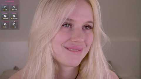 Media: Video of a smiling, fair-skinned, blonde woman with long hair, wearing a light-colored top. Background shows a weather forecast with temperatures.