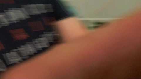 A blurred video shows a person in a black and white checkered shirt, with focus on the upper torso and arms. The background is indistinct, featuring a greenish hue.