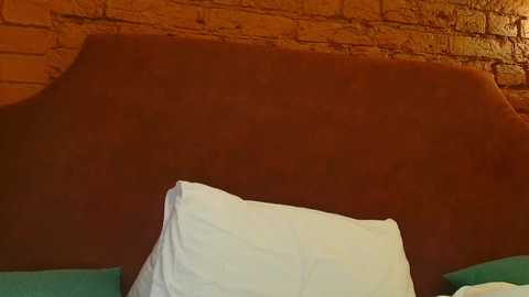 Video of a bed with a brown headboard and white pillows against a brick wall, creating a cozy, rustic ambiance.