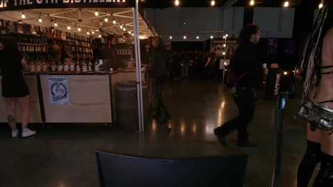 Video of a dimly lit bar with a bartender behind a counter, patrons seated at tables, and a person in black walking by.