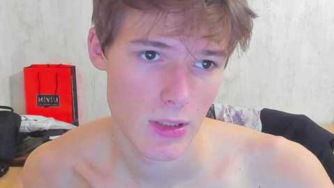 A video of a shirtless young man with short brown hair, light skin, and wide eyes, looking surprised or shocked. Background includes a red box and a white wall.