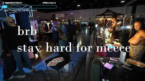 Media: Video of a crowded, dimly lit convention hall. A topless woman with large breasts stands behind a booth selling merchandise. Text reads, \"bro stay hard for meee.\