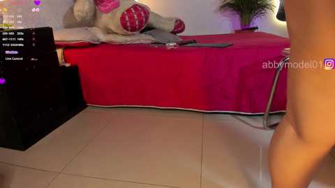 A video showing a nude person's bare buttocks in a room with a red bed and a large stuffed teddy bear, with a computer screen displaying a live stream.