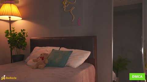 Video of a dimly lit bedroom with a wooden bed, a teddy bear, and a potted plant; wall art and a lamp provide a warm ambiance.