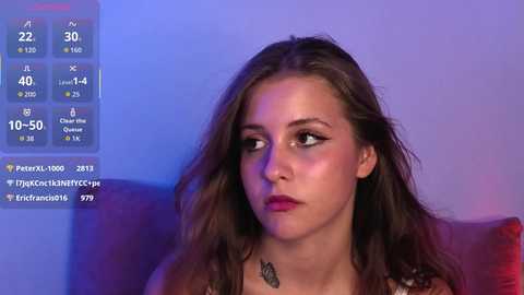 Media: Video of a young woman with long brown hair and dark lipstick, seated indoors against a blue background, with a live stream overlay displaying social media followers and streaming stats.