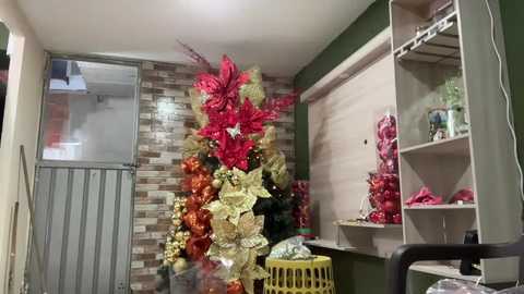 Video of a festive room with a tall, vibrant Christmas tree adorned in red, gold, and green decorations. The background features a wooden wall and a metal door, with shelves holding more festive items.