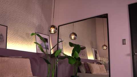 Video of a modern, minimalist living room with lavender walls, a mirrored wall, a beige sofa, a potted plant, and three spherical pendant lights.