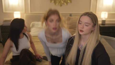 Video of three women in a dimly lit bedroom: two seated, one standing, all with shocked expressions.