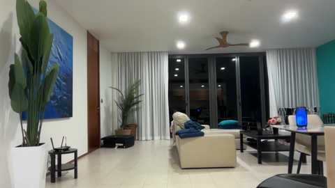 A modern, minimalist living room with light wood flooring, beige couch, blue throw, black dining chairs, and a turquoise wall.