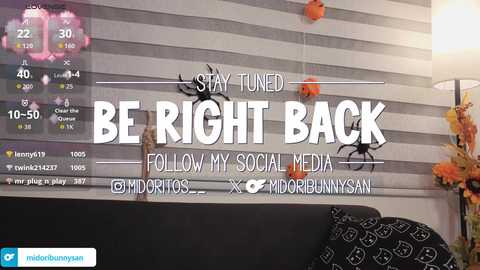 Video of a living room wall with a \"Stay Tuned\" banner, featuring social media handles, a digital clock, and a decorative spider.