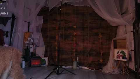 Video of a dimly lit, cozy bedroom with a wooden backdrop, white sheer curtains, a bed with a textured blanket, and a small speaker on a stand.