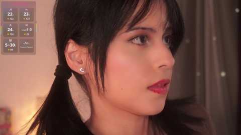 A video of a young woman with medium skin tone, black hair, and red lipstick, wearing a black top, against a blurred background.