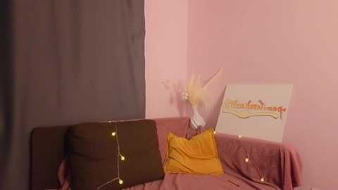 Media: A video of a cozy, pink-walled room with a brown couch adorned with yellow and brown pillows, a white sign reading \"Crazy Crayon\" on the wall, and string lights draped over the furniture.