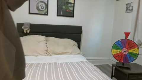 Video of a minimalist bedroom with a bed, striped bedding, a colorful spinning wheel toy, and framed pictures on the wall.