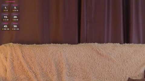 A video of a cozy bedroom with a plush, beige faux fur blanket covering a bed, set against deep purple curtains. A weather app shows the temperature at 45\u00b0F with a 50% chance of rain.