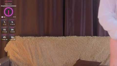 A video of a man in a white shirt standing beside a beige towel-covered couch with dark curtains in the background. A virtual screen with a female avatar and various stats is visible.