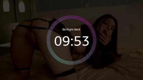 Video: A woman in black lingerie, bent over a bed, with a dimly lit room in the background. Text overlay: \"Be Right Back\" and \"09:53.\