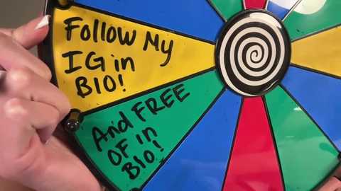 A video of a colorful, spiral-shaped game board with green, blue, yellow, and red sections. Hand holding the board, with the text \"Follow My IG in BIO!\" written in black on the yellow section.