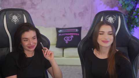 Video of two women in gaming chairs, one holding a controller, smiling, with a gaming pillow behind them.