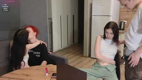 Video of a modern kitchen with three people: two women kissing, one man standing, and a laptop on a table.