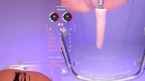 Video of a purple-tiled bathroom with a clear showerhead dispensing a light pink liquid into a transparent bathtub. The showerhead has digital controls and a person's arm is partially visible, indicating a human presence.