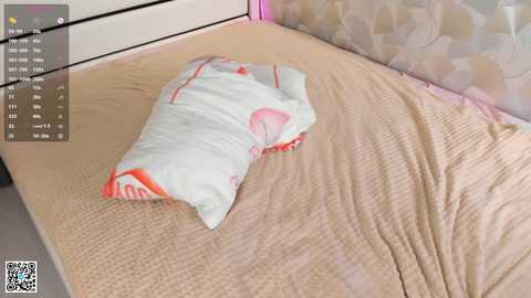 Video of a beige bed with a white pillow featuring a pink design and a matching pillowcase, set against a floral-patterned headboard. QR code and time stamp in the corner.