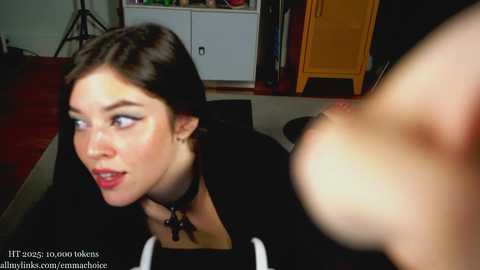 Video of a young woman with dark hair and red lipstick, wearing a black jacket and cross necklace, looking surprised.