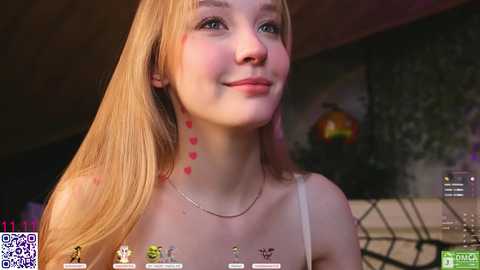 Media: A video of a young woman with long, blonde hair and fair skin, wearing a white tank top. Her face is lightly smeared with red, heart-shaped marks. The background features a dimly lit room with a decorative pumpkin.
