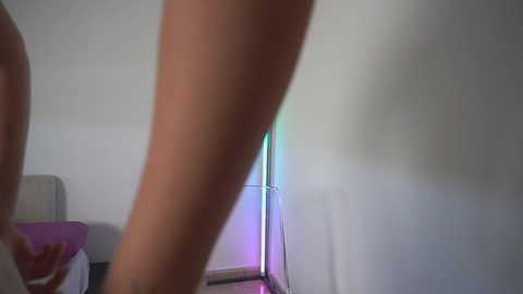 A video of a woman's bare, tanned legs standing in a dimly lit room. A purple lamp with a white shade and a colorful, abstract light pattern is visible in the background.