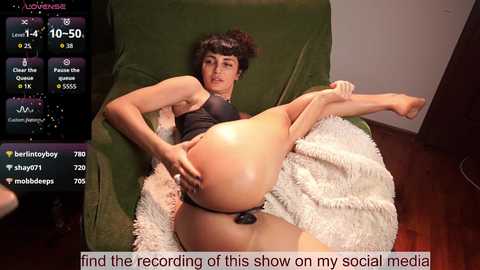 Video of a young, fair-skinned, brunette woman in a black bra, lying on a green couch, with a fluffy white blanket, and a black thong, with text overlay about her social media show.