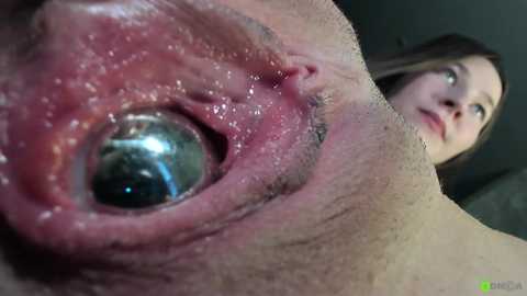 A close-up video of a woman's eye with a metallic ball inside, surrounded by a natural eye socket, with her face blurred in the background.