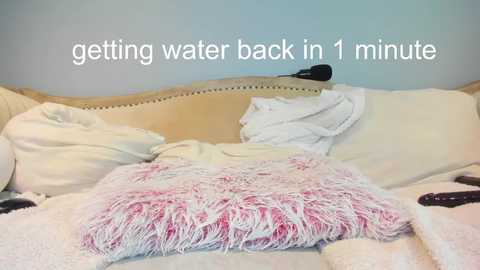 A video of a messy bedroom with a white bed, a fluffy pink pillow, and a white sheet, featuring text overlay: \"getting water back in 1 minute.\