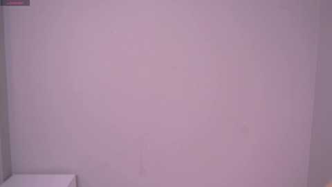 Video of a plain, off-white wall with subtle shadows and a corner of a white object, possibly a shelf or furniture, visible on the left. The image has a soft, muted color palette and minimalistic aesthetic.