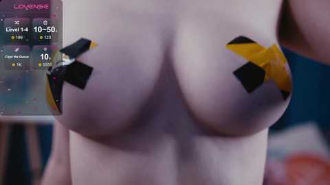 A video of a woman's bare chest covered with yellow and black duct tape \"X\" patches, with a game overlay showing health, level, and other stats.