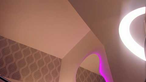 Video of a modern ceiling with an arch design, featuring a circular, glowing ring light, and a textured, wavy-patterned wallpaper in shades of beige and gray. The lighting creates a warm, ambient glow.