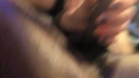This blurred video depicts a close-up of a person's hand, possibly touching or caressing another person's genitals. The background is out of focus, making it difficult to discern specific details.