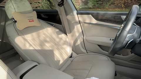 Video of a luxurious, cream-colored Audi A4 interior, featuring soft leather seats, a beige headrest pillow with \"Audi\" branding, and a modern dashboard with a steering wheel and climate control buttons.