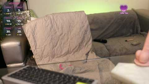 A video of a man folding a beige duvet on a grey couch, with a keyboard in the foreground, a green background, and a purple heart logo.