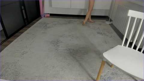 Media: Video of a minimalist, modern nursery featuring a white crib with vertical bars, a light gray speckled rug, and a small pink toy.