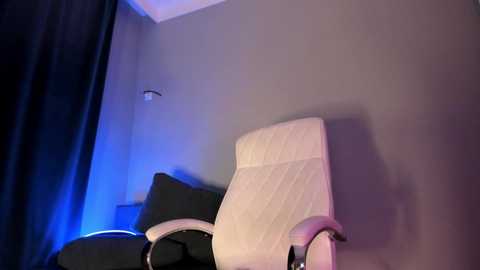 Video of a modern office chair with a white mesh backrest and black leather seat against a gray wall, illuminated by blue ambient light.